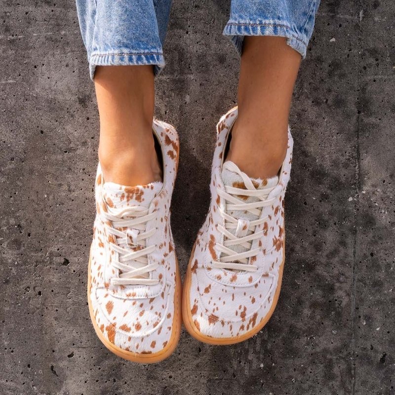 Mukishoes calf skin cow print wide toe box sneaker being worn by a person with their feet resting against a cement wall