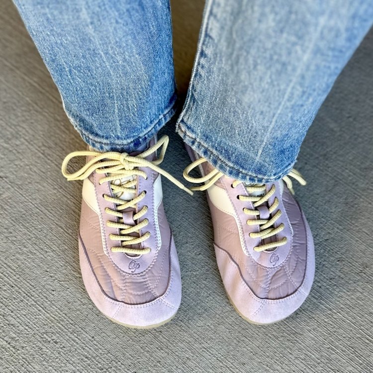 A pair of light purple Sneakerina shoes from Ohne Project. They are a quilted textile material with pale yellow laces shown here with medium wash denim
