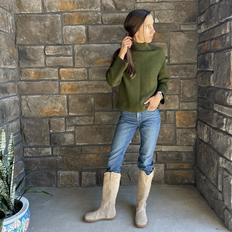 Full body view of a woman in jeans and a dark green sweater, jeans, and Shapen Arizona beige western inspired barefoot tall suede boots with a wide toe box