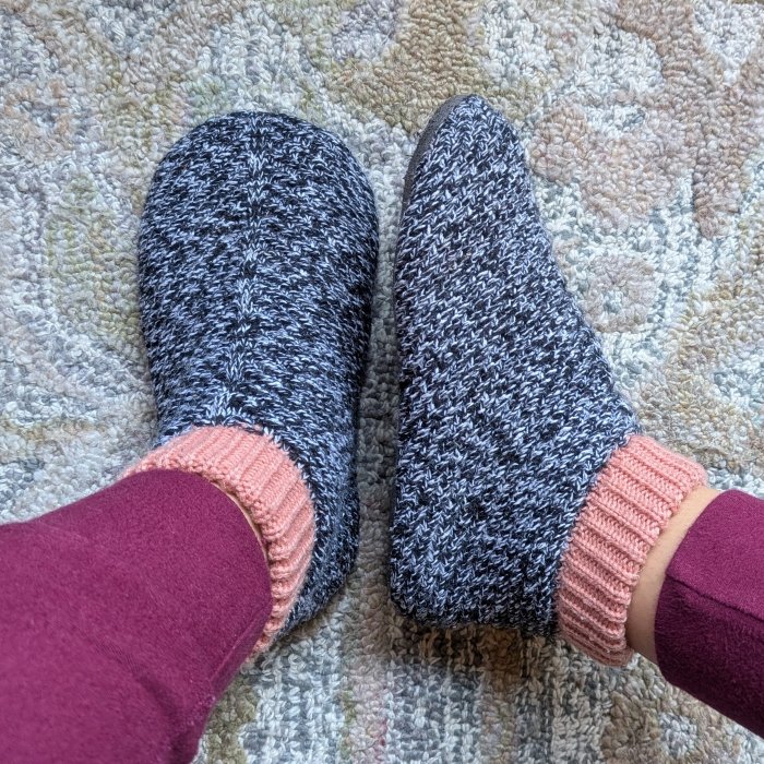 A close up top and side view of a pair of knit deadstock yarn booties with a wide toe box in a marled gray pattern with pink cuffs.