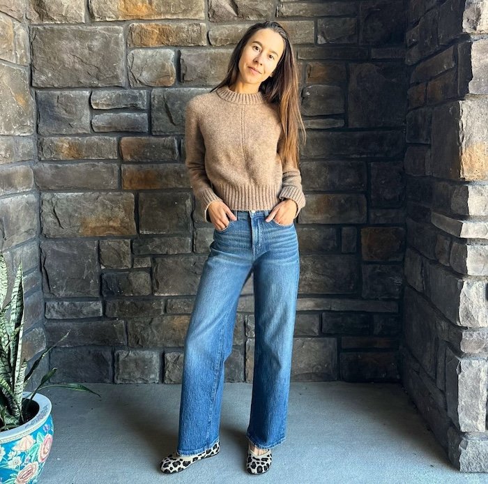A woman smiling at the camera wearing a sweater, denim, and Xero Shoes Leopard print phoenix barefoot knit ballet flats