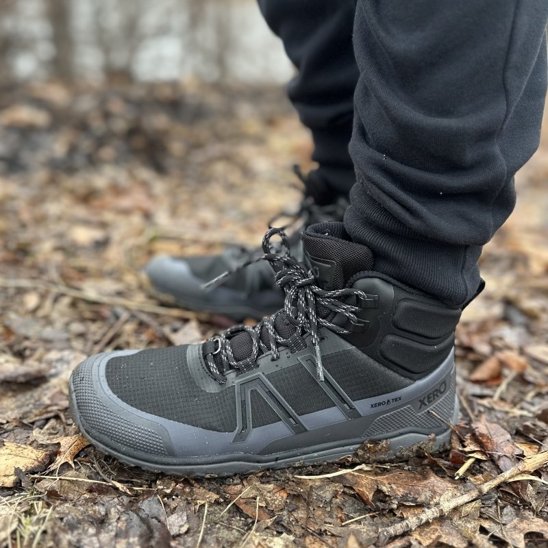A side view of a pair of legs in Xero Shoes Scrambler Trail Mid Waterproof barefoot hiking boots being worn on leaf covered ground