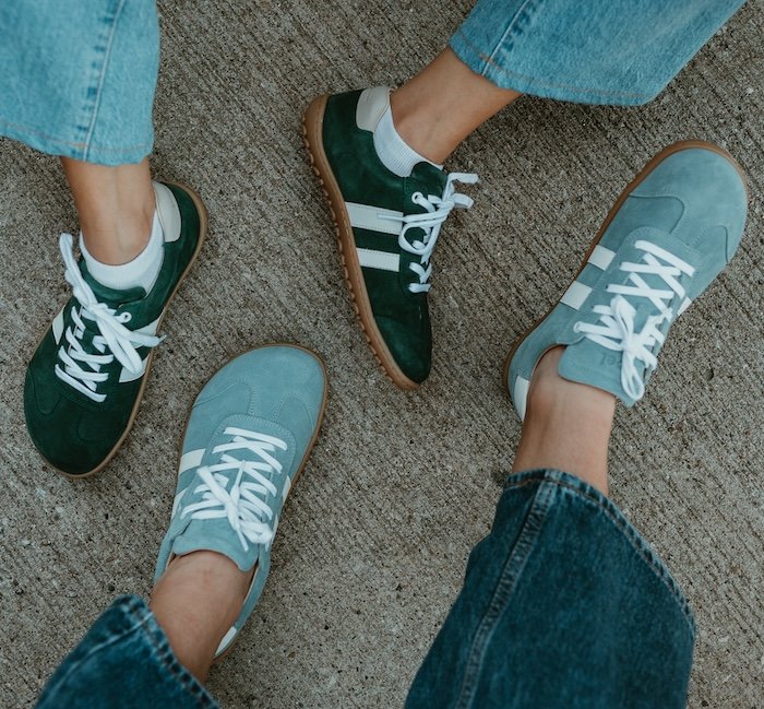 a top down view of two people's feet in Koel Ila Suede in two colorways. Dark green and light blue barefoot wide toe box sneakers