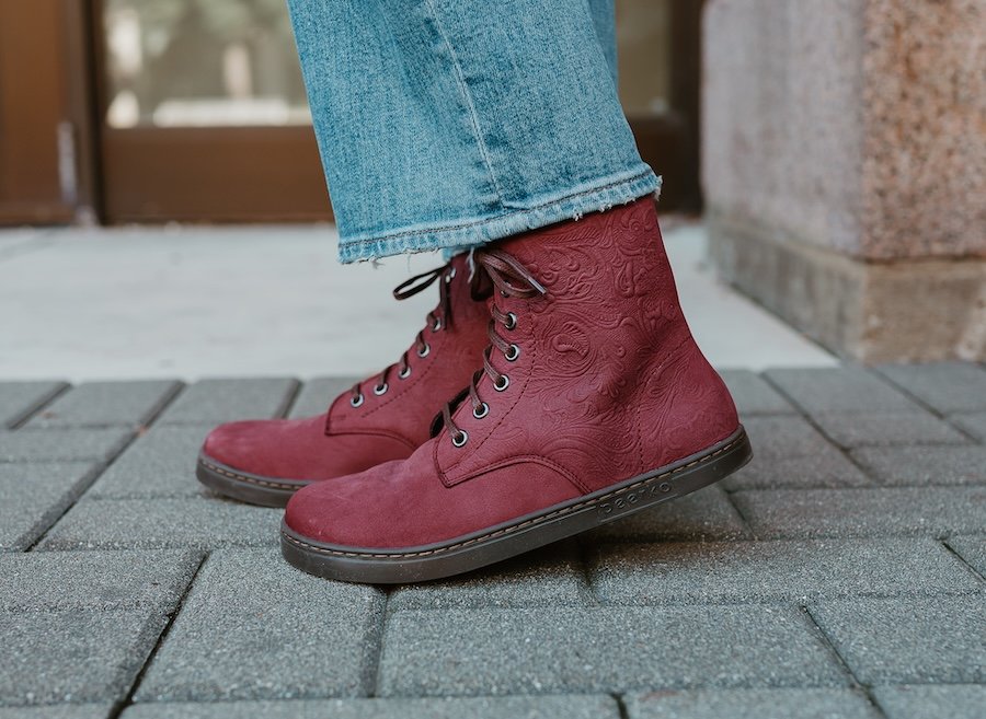 A side view of Peerko Go in Maroon with embossed details being worn by a person on a brick pathway. The zero drop outsole is being flexed up slightly on the boot in front