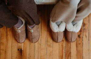 A top down look at two people in lounge pants and Zeazoo sheepskin barefoot slippers with wide toe boxes against a hardwood floor