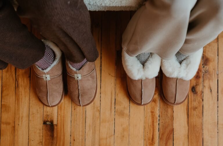 A top down look at two people in lounge pants and Zeazoo sheepskin barefoot slippers with wide toe boxes against a hardwood floor