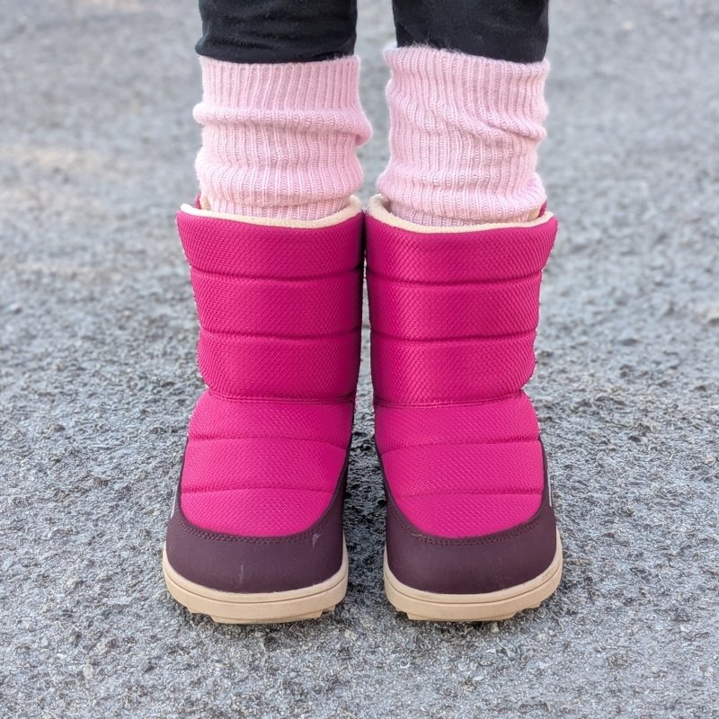 A front view of a young girl in Be Lenka Kids Ailo Snow Boot in Berry pink being worn with pink socks. The extra wide toe box boots are warm and thick.