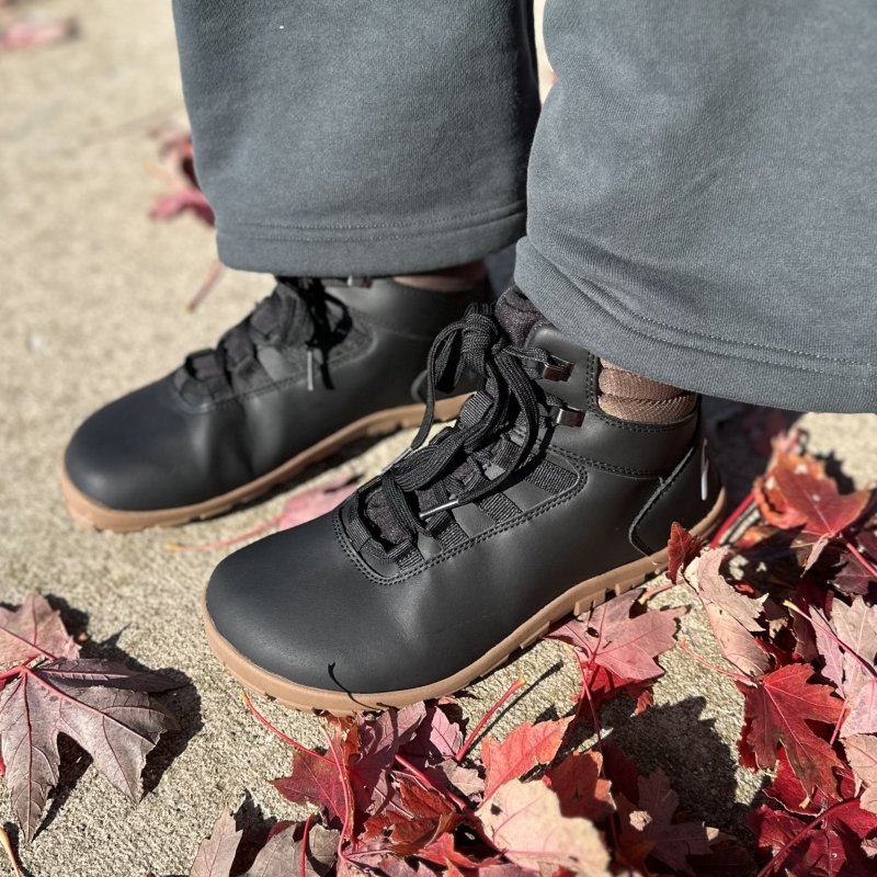 Close up view of a pair of feet in Freet Barefoot Arken 2 insulated warm barefoot winter boots. The person has on wide leg sweatpants and is standing near red fall leaves.