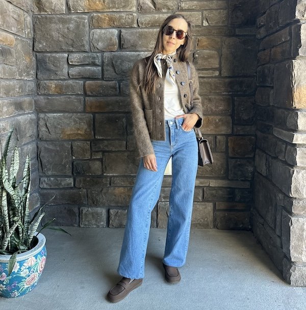 A woman standing wearing light blue denim, Groundies barefoot loafers, smiling at the camera.