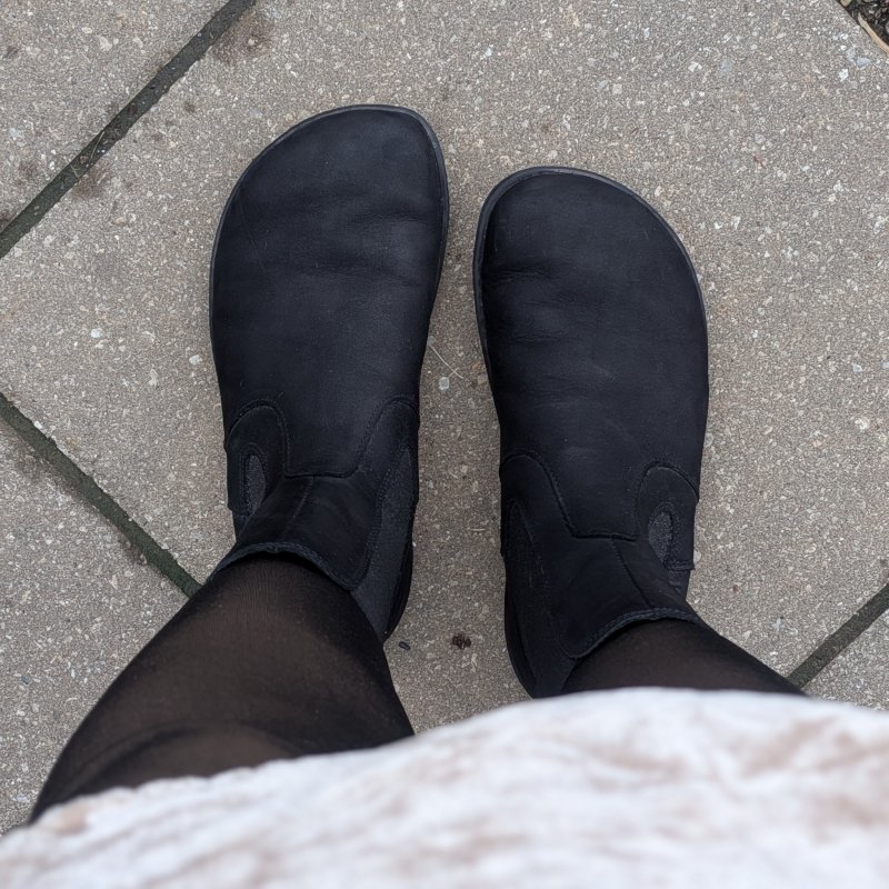 Top down close up of a pair of extra wide toe box chelsea boots from Groundies. The Camden in Barefoot+ offers extra toe room and is shown in black suede worn with black tights and a champagne velvet dress