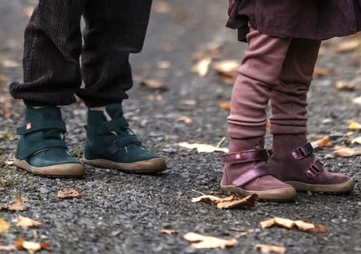 A pair of children visible from the legs down standing in the street with fallen leaved around wearing Lang.S warm barefoot winter boots for kids
