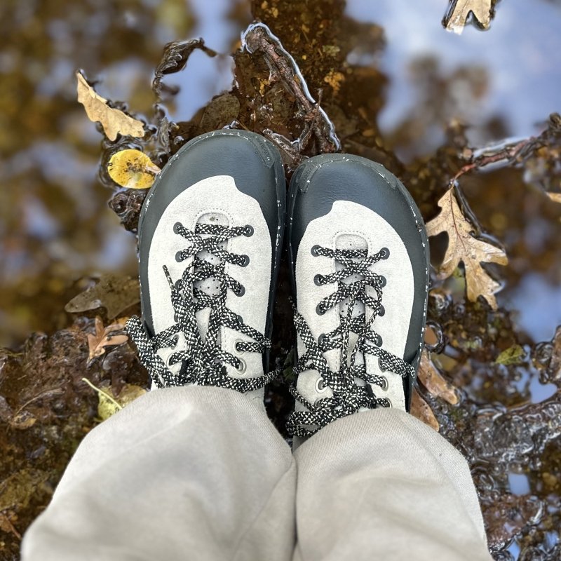 top down look at a pair of Lono Wild barefoot hiking shoes standing on wet muddy ground. The wide toe box has a covered toe guard.