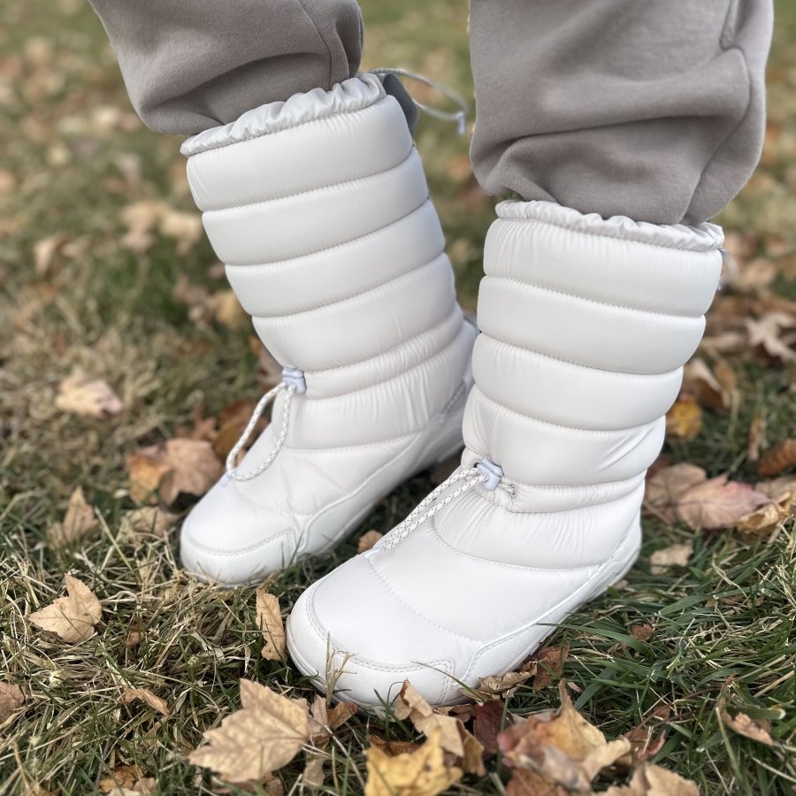 A close up of a pair of white Xero Alpine pull on warm snow boots with a wide toe box.
