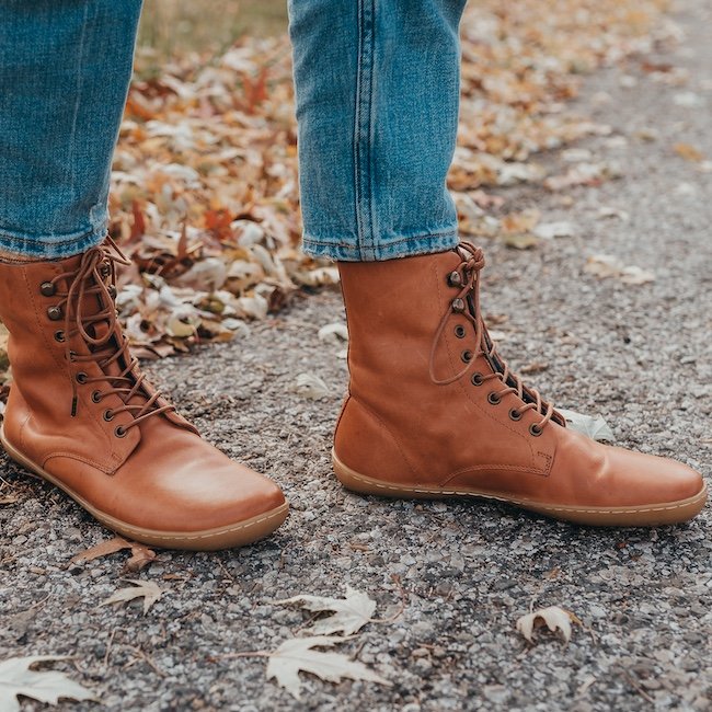 A close up view of a pair of feet standing outside wearing Mukishoes Alentejo brown leather lace up barefoot boots
