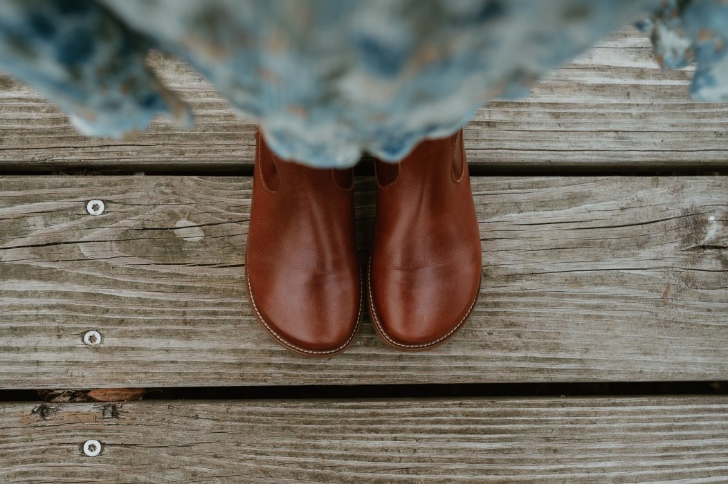 A top down close up view of a pair of Faye Boots by Anya in Cognac, a smooth brown barefoot booth with stitching details.