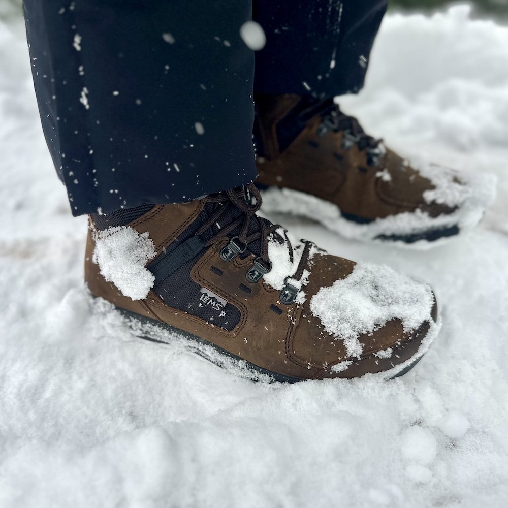 Side close up of a pair of Lems Insulated Brek winter barefoot boots with a wide toe box being worn outside on very snowy ground