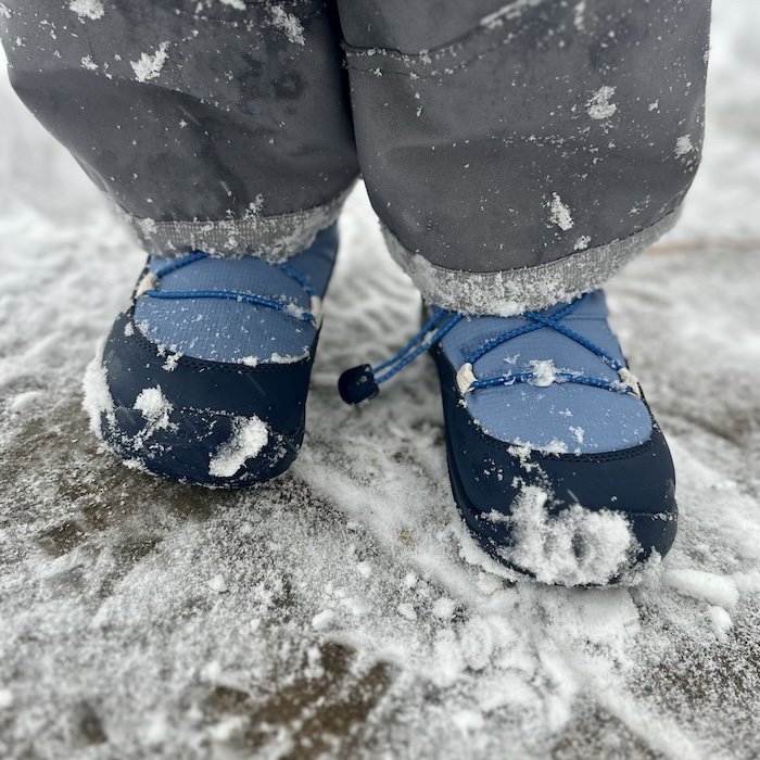A front close up view of a young child in Reima Ensilumi barefoot winter boots worn on snowy ground