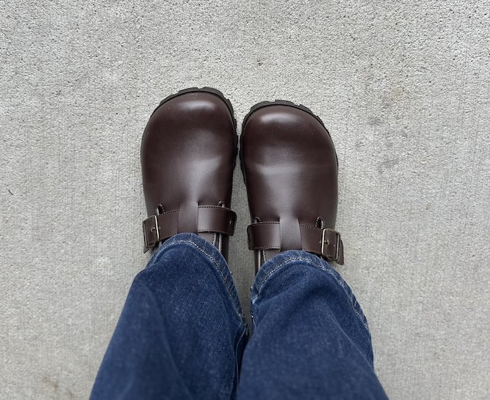 Top down look at a pair of Barebound Ikarus barefoot clogs in dark brown being worn with dark denim. The top down view shows the wide anatomical toe box