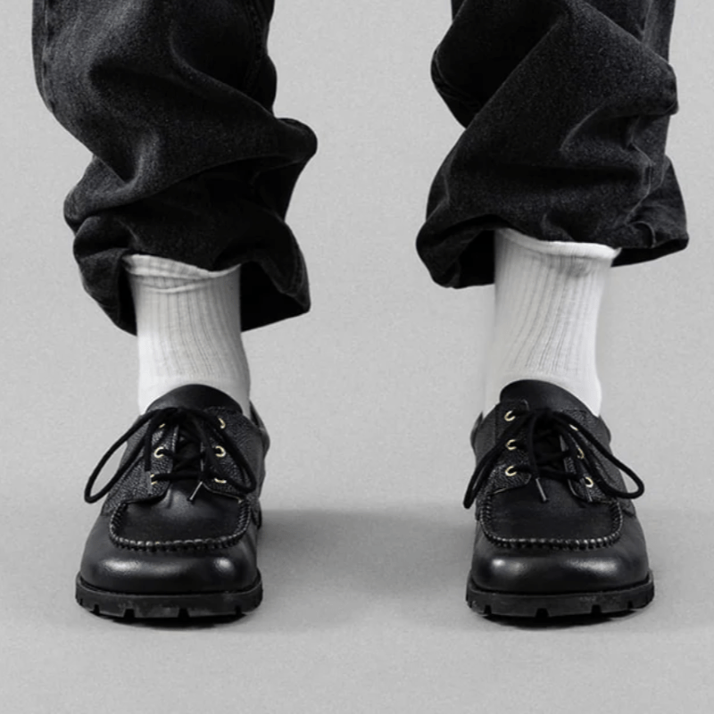 Front view of a person's feet in Barebound Orpheus boat shoes with a wide toe box. They are styled with tall white crew socks and black denim tucked in.