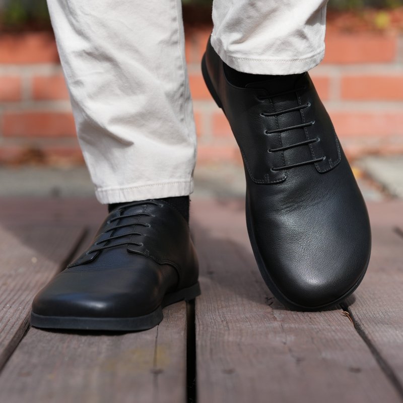 A close up view of a person walking in black leather barefoot wide toe box Jefferson dress shoe from Oaka Studio