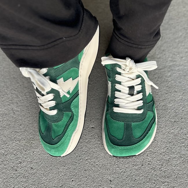 Top down view of wide toe box Dolfie Paradise sneakers in shades of green with a retro vibe. The foot on the left is tilted up slightly to show the faux heeled zero drop sole.