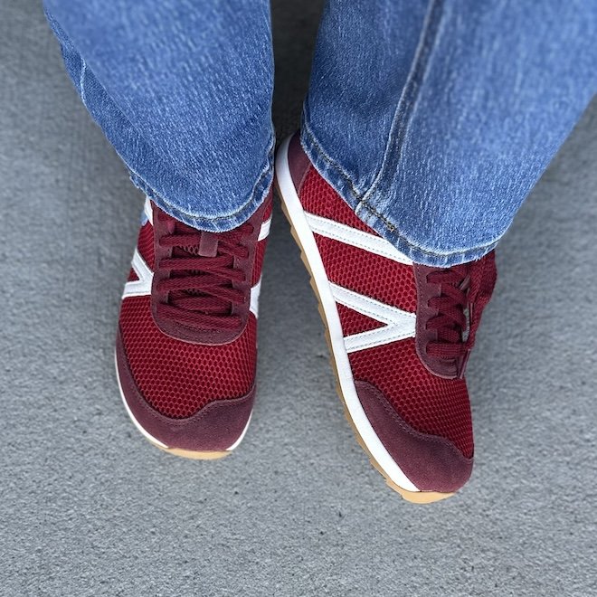 A close up top down front view of a pair of Xero Wynn retro style barefoot sneakers in red mesh with white straps. The right foot is tiled up to show the side, and the left is flat is highlight the wide toe box.
