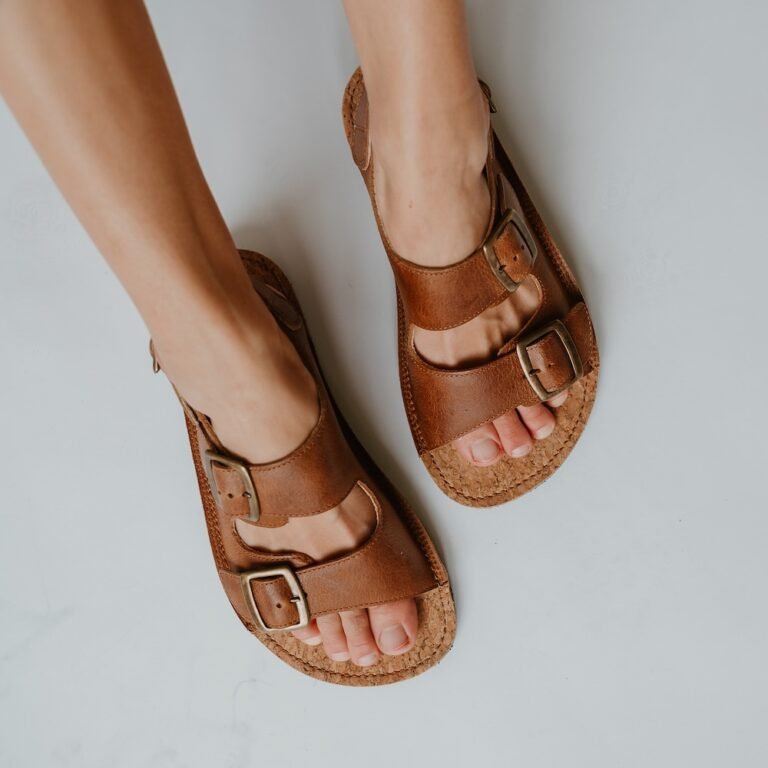 Top down close up of a person's feet in Koel Ada, a Birkenstock style double strap brown leather sandal with a wide toe box.
