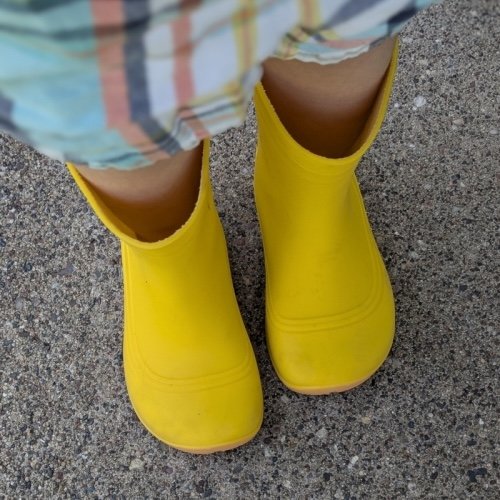 A top down view of a child's feet wearing Be Lenka Pudds kids wide toe box barefoot rain boots in yellow rubber.