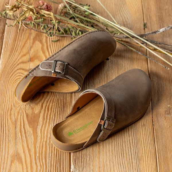 A close up view of a pair of El naturalista leather clogs resting on a wood floor, showing the anatomical shape and cushioned footbed