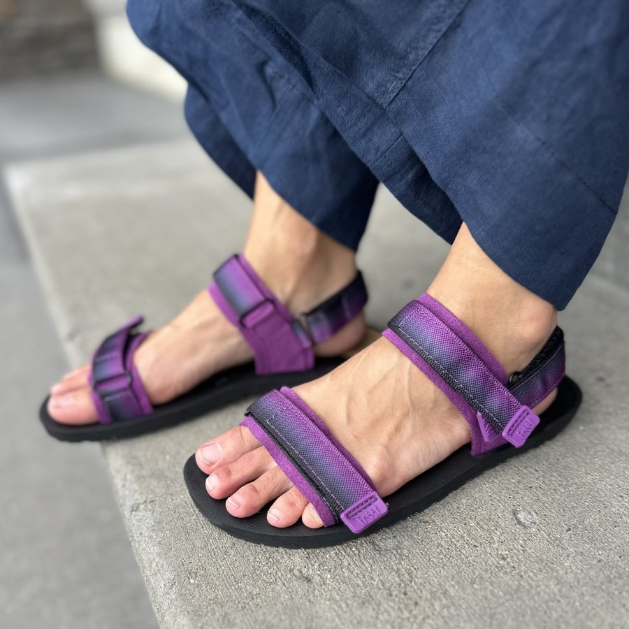 A side view of a person's feet in Freet Lundy double strap barefoot sandals in a pink to gray gradient color.