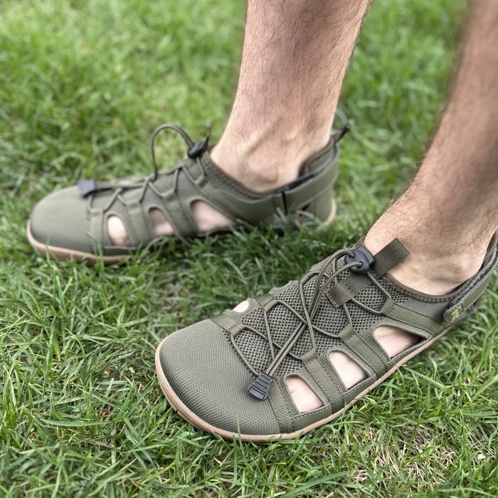 A side angle close up view of a person's feet in Freet Barefoot Zennor closed toe barefoot sandals in olive green mesh with elastic cinching laces.