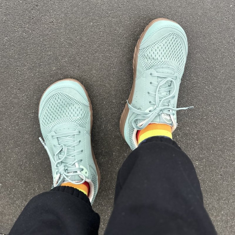 Top down look at a person's feet in Primal Zen barefoot minimalist sneakers with a wide toe box in Mint colored mesh. Rainbow socks are peeking out under black sweatpants and the rigth feet is angled slightly.