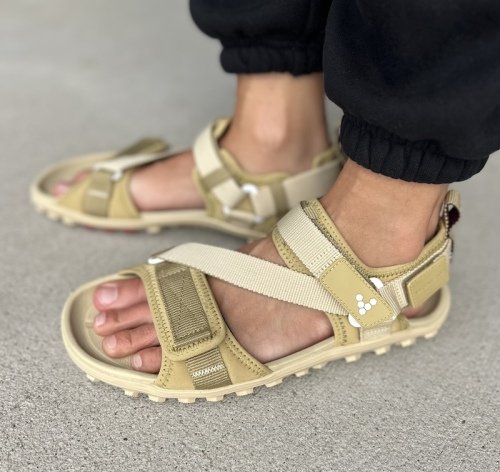 A side close up view of a person's feet in Vivobarefoot Tracker Ora adventure barefoot sandals with adjustable straps in a beige green colorway.
