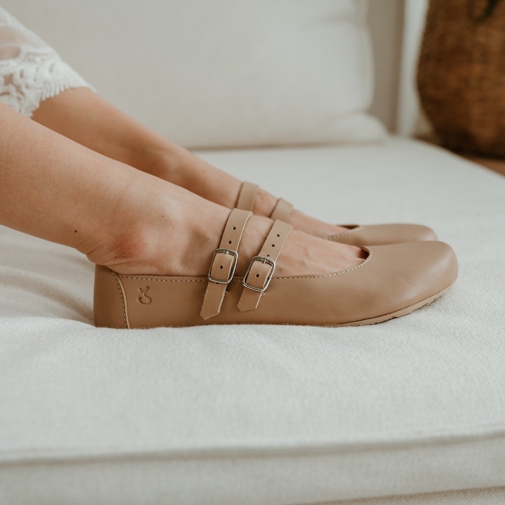 A pair of Jenon Leather Villet double strap mary janes in a light tan leather shown from the side resting on a white couch.
