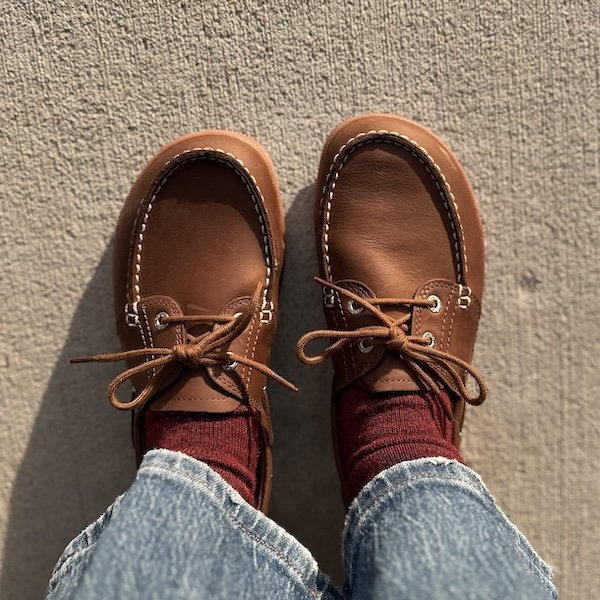 A pair of Baer boat shoes with a wide toe box and supportive outsole being worn outside in the fading sun. They are brown leather with white stitching and brown laces.