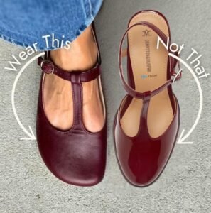 Annotated image of a pair of t-strap red patent pumps next to a pair of Origo T-bar flats with a wide toe box. An arrow with the words Wear This is pointing at the Origo flat, and an arrow with Not That is pointing at the conventional almond shaped toe box.