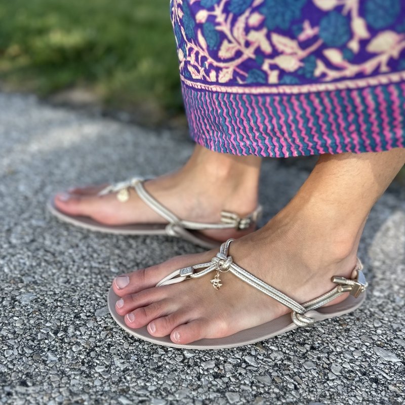 Side view of a woman wearing a patterned skirt paired with a pair of Xero Shoes Genesis gold leather barefoot strappy sandals.