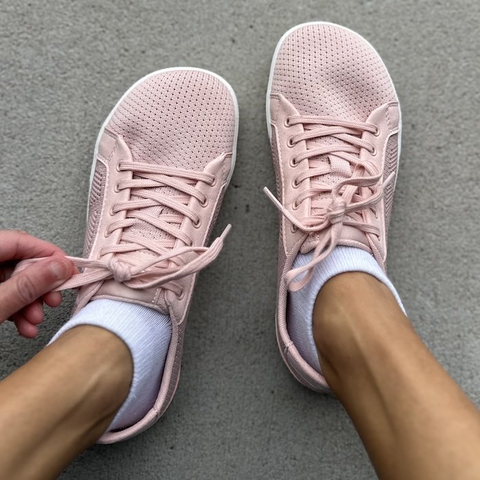 A close up top down view of a pair of feet standing on pavement wearing Xero Shoes Dillon Knit casual women's barefoot sneakers in dusty pink