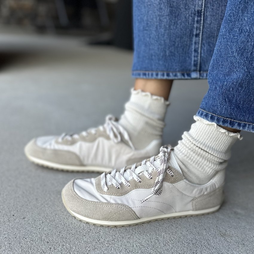 Side view of a person's' feet in Zara Barefoot sneakers with patterned laces and a white and gray colorscheme. The flat zero drop outsole is visible under the wide toe box sneaker.