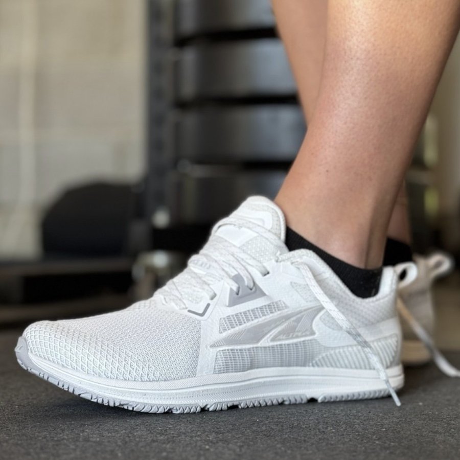 Side view of a woman's feet in white Altra Solstice XT 3 sneakers with a wide toe box and flat flexible outsole