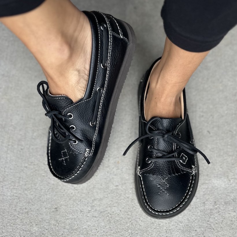 Top down and tilted view of a pair of black boat shoes from Dolfie Paradise with a wide toe box, laced edge, and stitching details