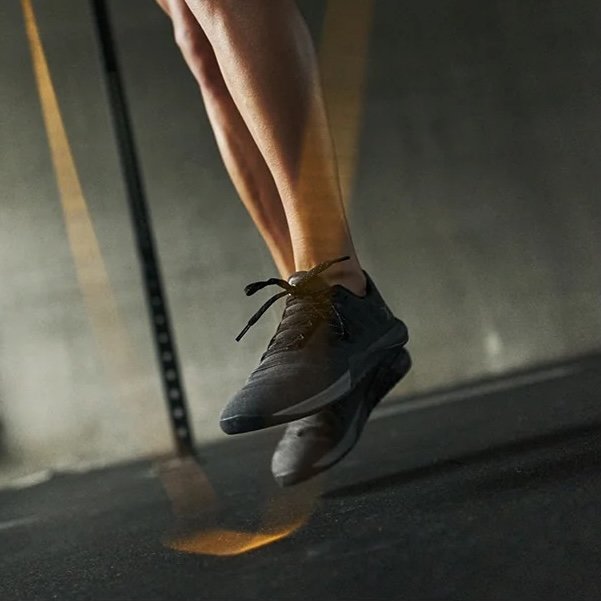 A close up of a person visible from the knees down mid-jump over a gym floor wearing Flux Footwear Adapt Graphene wide toe box gym shoes in all black
