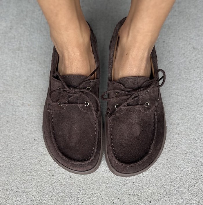 Close up top down view of a person's feet in wide toe box Hivera boat shoes from Koel in dark brown suede