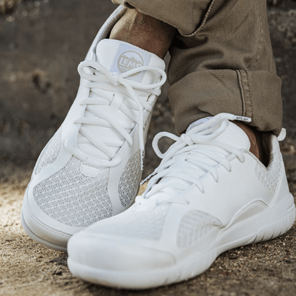 Close up of a pair of crossed feet in white mesh Lems Primal 3, a wide toe box cushioned sneaker for training and casual use.