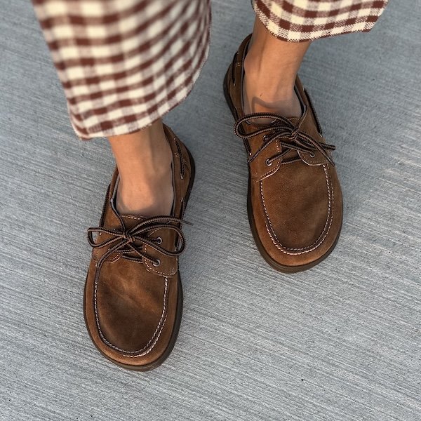 A top down view of a person's feet in a pair of Magical Shoes Galeon, a wide toe box boat shoe. A pair of brown plaid pants are visible at the top of the frame