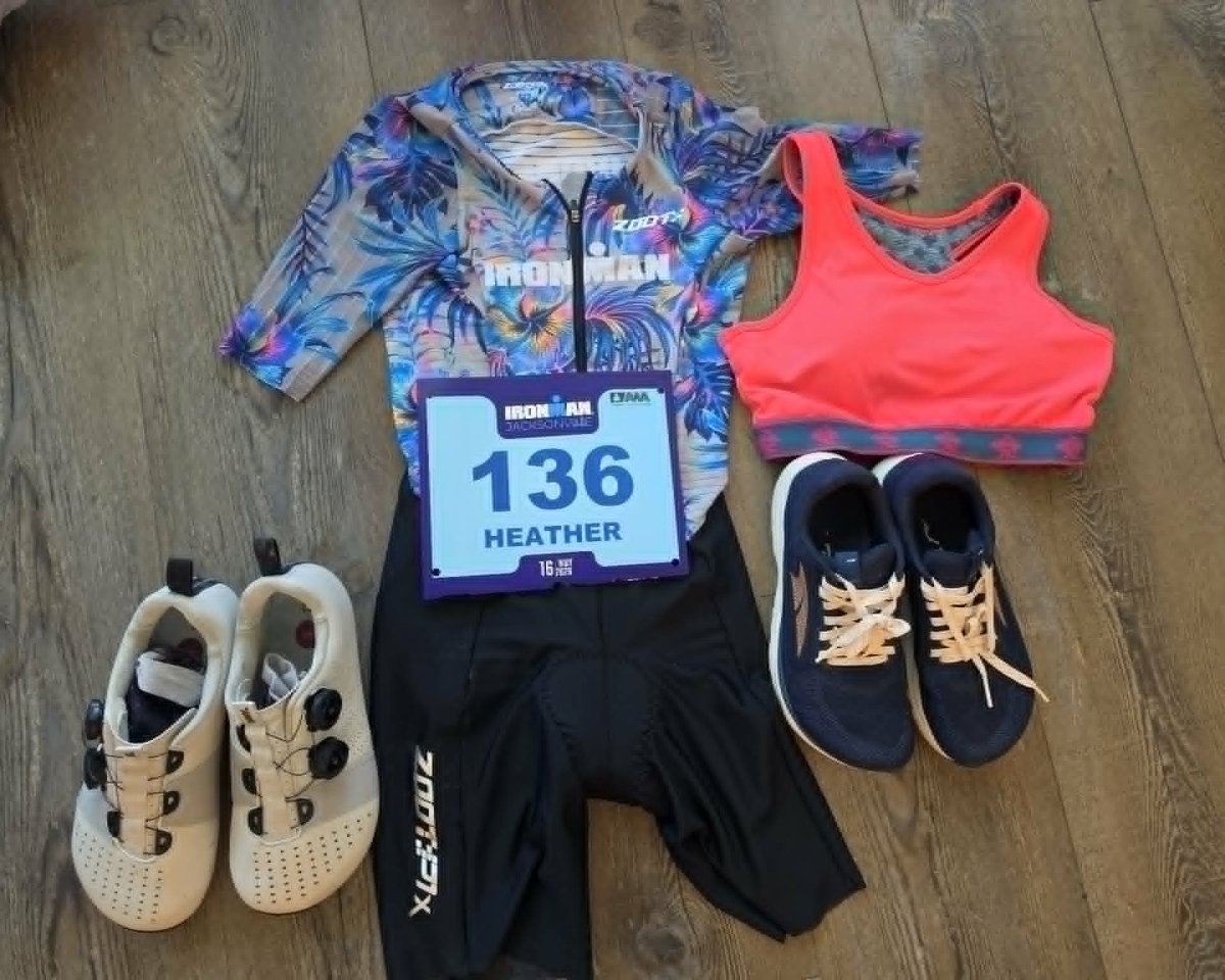 Flat lay showing ironman gear ready for race day, including a bib number 136, sports bra, cycling shorts, altra running shoes, and Strong Feet Athletics leviathan wide toe box cycling shoes