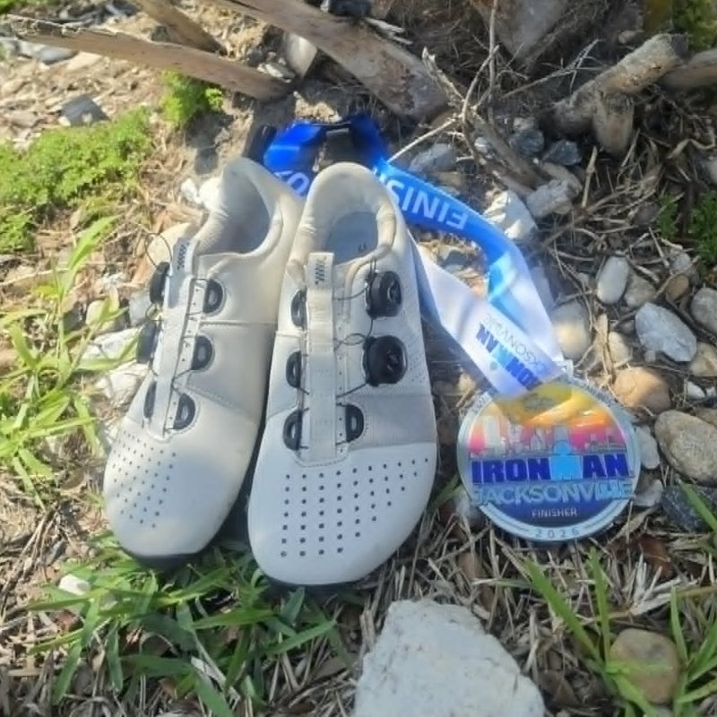 A pair of Strong Feet Athletics Leviathan foot shaped cycling shoes on the ground with an Ironman jacksonville finisher medal next to them