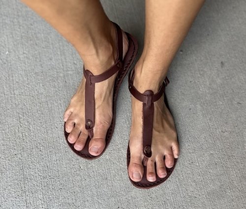 A front view of a person's feet in Common Tread brown leather women's barefoot sandals with a toe post and ankle strap