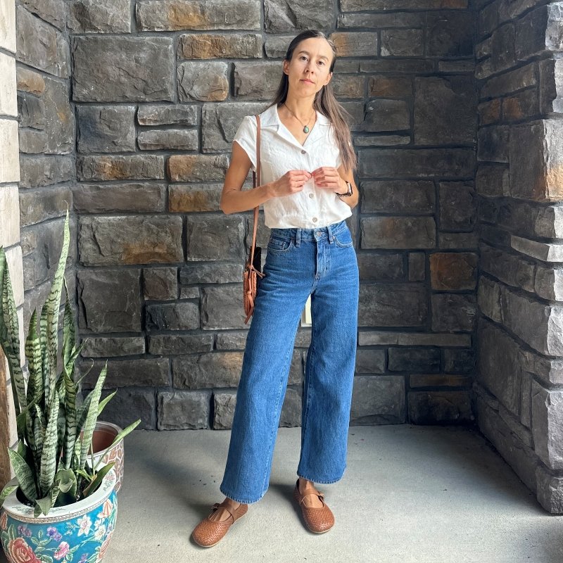 Full body image of a woman in jeans, a white button down top, a woven leather bag, and a pair of Origo Intreccio woven leather mary janes that match.