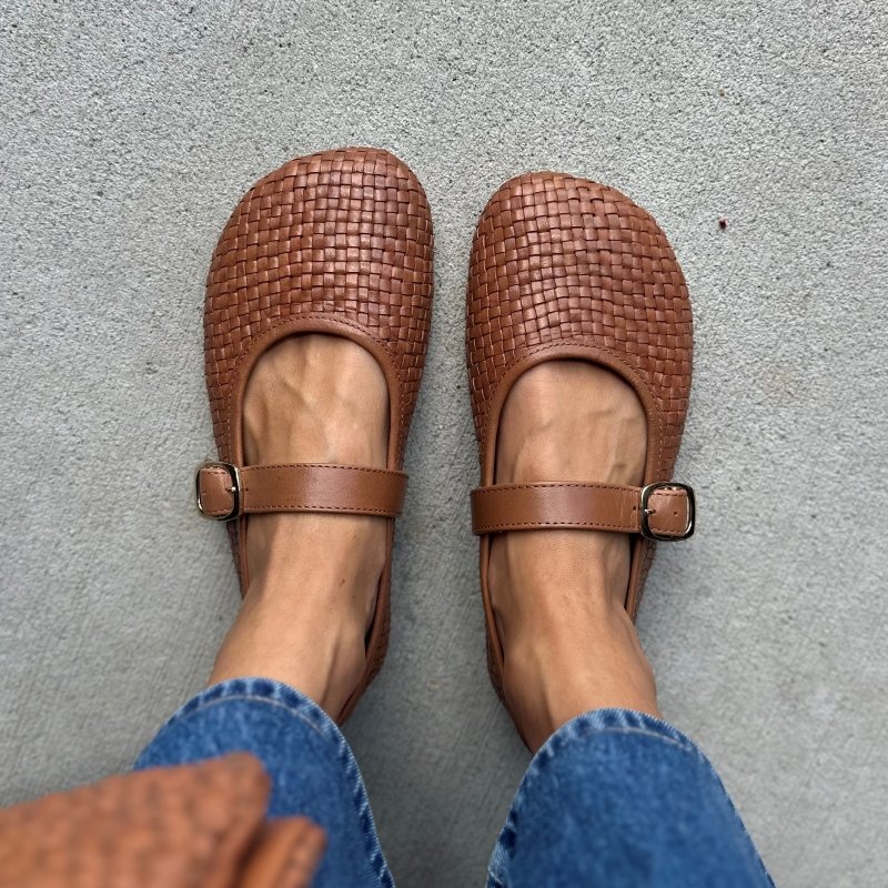 Top down look at a pair of Origo Intreccio, a woven leather mary jane in a medium brown. The matching leather bag is just visible blurred at the bottom of the photo.